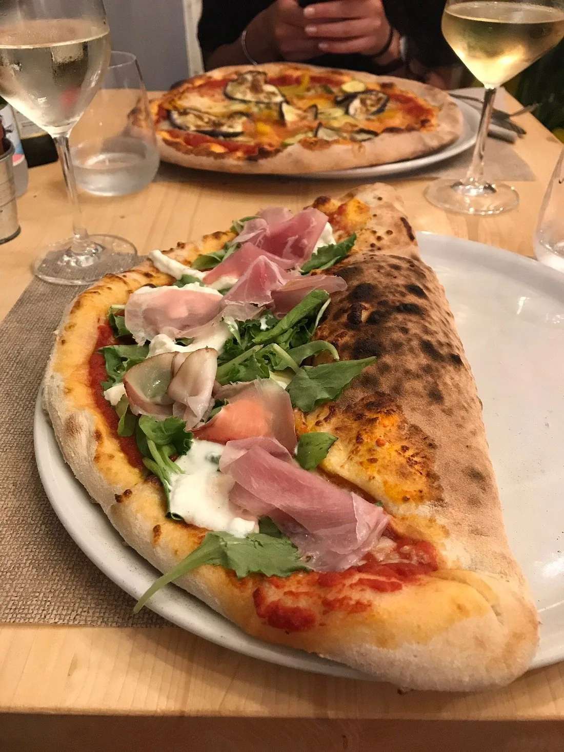 Calzone met&agrave; chiuso e met&agrave; aperto: da un lato il calzone dorato, dall&rsquo;altro pomodoro, rucola, prosciutto crudo e stracciatella.