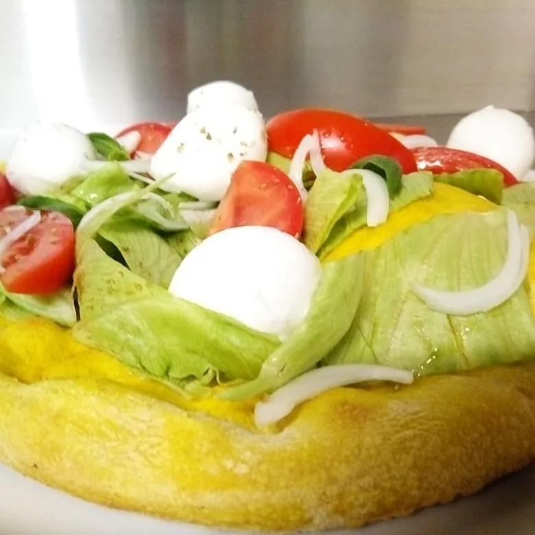 Pizza con impasto giallo, condita a crudo con insalata, mozzarelline, pomodorini e cipolla.