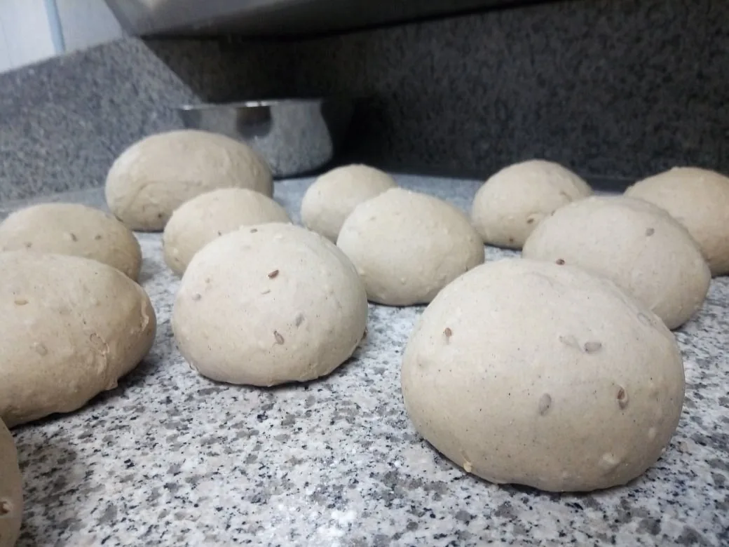 Panetti di impasto multicereale in lievitazione su un banco di granito infarinato.