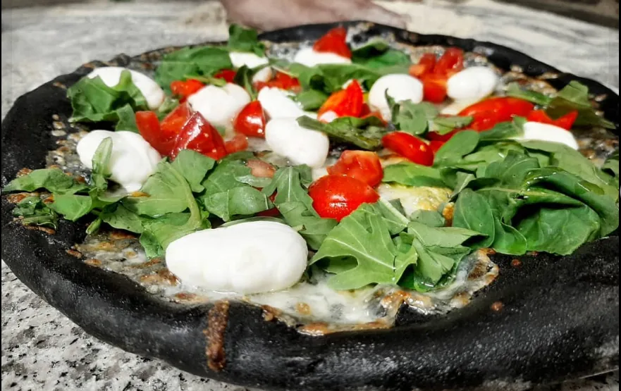 Pizza con impasto al carbone vegetale, base nera con pomodorini, rucola e mozzarelline di bufala.