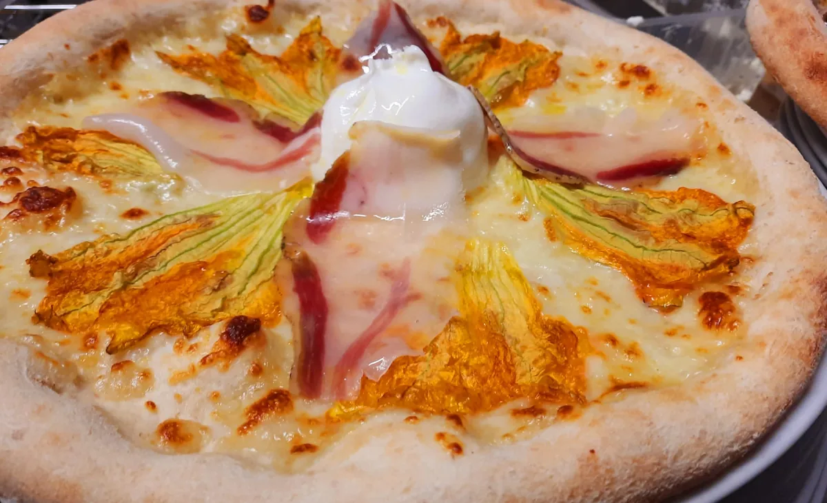 Pizza bianca con fiori di zucca, prosciutto crudo e una burratina al centro.