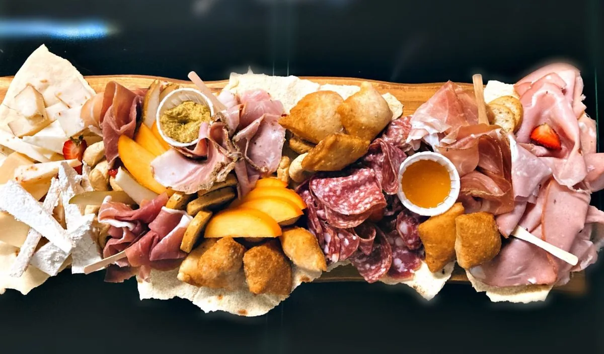 Tagliere lungo con salumi, formaggi, fritti e composte, servito su pane carasau.