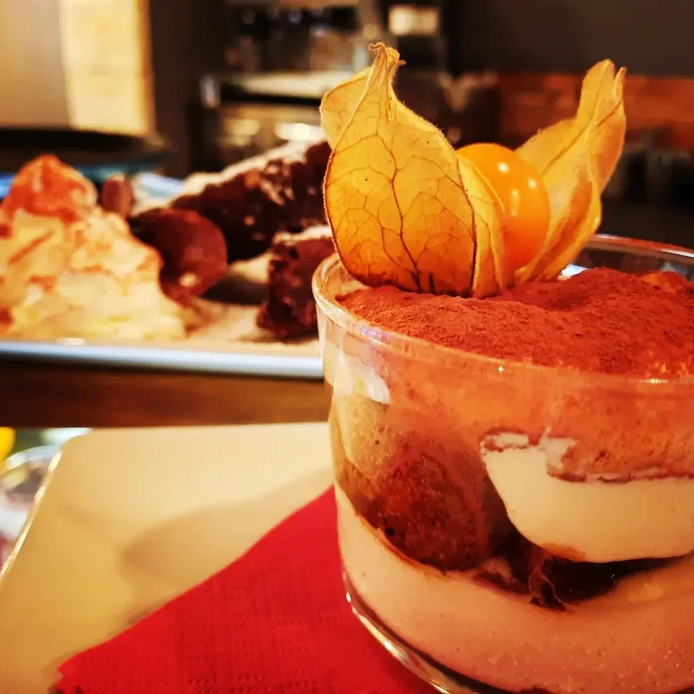 Tiramis&ugrave; servito in un bicchiere, con un alchechengi appoggiato sopra.